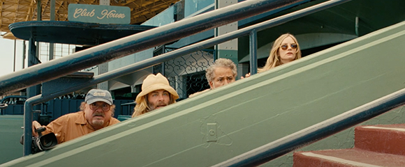 Four people look out from behind a green railing at a clubhouse.