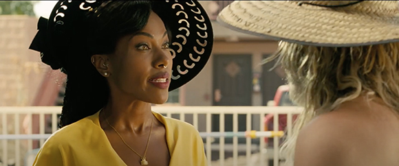 A woman in a yellow top and large black sun hat looks toward a blonde woman wearing a straw hat.