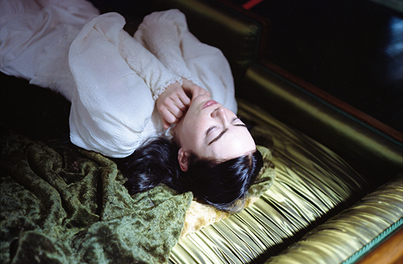 A person in a white blouse lying with eyes closed on a textured surface.