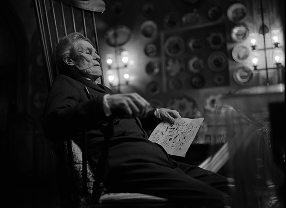 Black and white photo of a man in a suit sitting in a chair and holding a piece of paper.