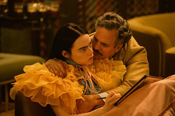 A man with graying hair leans in to embrace a woman wearing a voluminous yellow ruffled top.