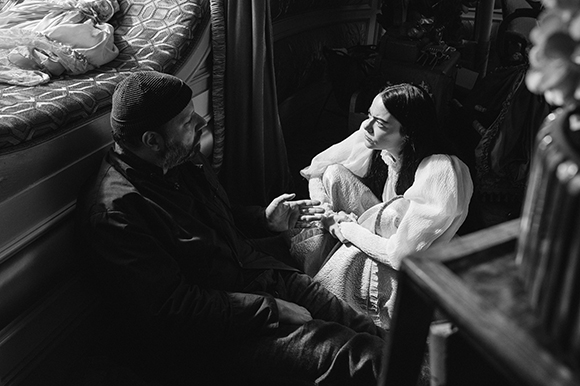 Black and white photo of a man and a woman sitting on the floor in a dark, vintage-style room.