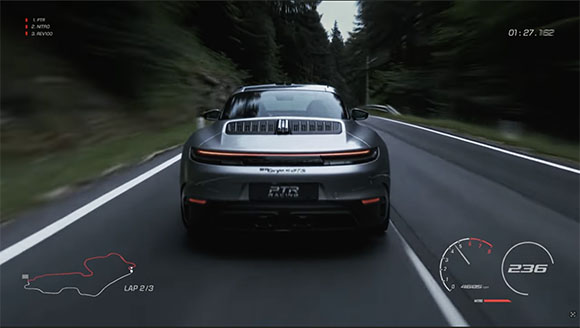 A gray sports car driving fast on a paved road through a dense forest.