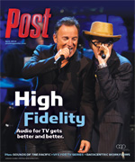 Bruce Springsteen and another man in hats sing into microphones on a stage with blue lighting.