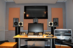 A recording studio desk with monitors, speakers, a large screen, and audio equipment.