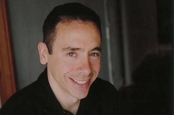 A man with short dark hair and a slight smile looking toward the camera.