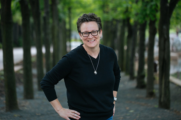 A smiling woman with short dark hair and glasses wearing a black long-sleeved shirt in a park.