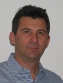 A man with short dark hair wearing a blue and white striped button-down shirt.