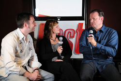 A man in a white shirt, a woman in black, and a man in a blue shirt sit together holding microphones.