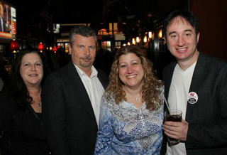 Four people posing together and smiling at an outdoor evening event.