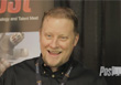 A smiling man with light hair wearing a black button-down shirt and a lanyard.