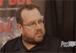 A man with short hair, glasses, and a beard wearing a black shirt looking off-camera.
