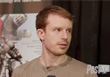 A man with reddish-brown hair and a mustache looking off-camera against a blurred background.