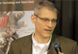 A man with short gray hair and glasses wearing a blazer speaks into a microphone.
