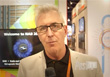 A man with grey hair and glasses wearing a light grey blazer and black shirt.