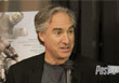 A man with graying hair wearing a black jacket speaks into a microphone.