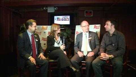 Four people sit in a row on a stage during a panel discussion in a dimly lit room.