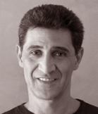 Black and white close-up portrait of a man with dark hair smiling.