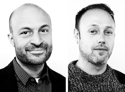 Black and white close-up portrait of two men looking at the camera against a white background.