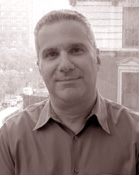 A man with short hair wearing a button-down shirt, looking forward against a blurred city background.