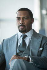 A man with a goatee wearing a grey three-piece suit and a dark tie, looking to the side.