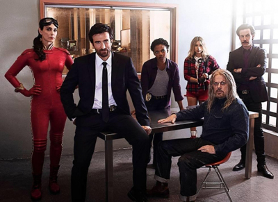 Seven people in various costumes and formal wear pose together in a room with a large mirror behind them.