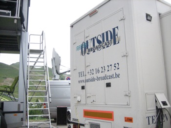 White outside broadcast truck with satellite dish, phone number +32 16 23 27 52, and website www.outside-broadcast.be.