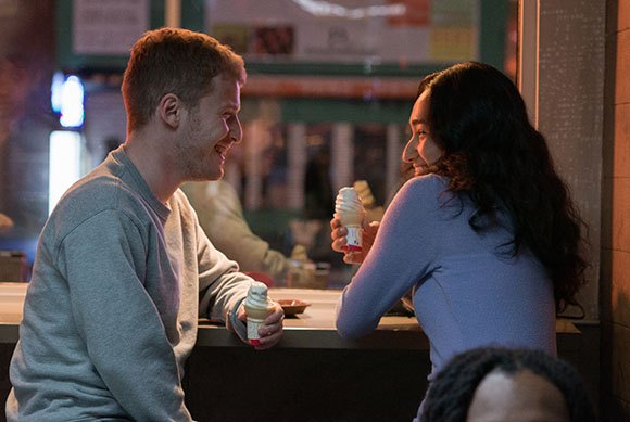 A man and a woman sit at a counter, smiling at each other while holding soft-serve ice cream cones.