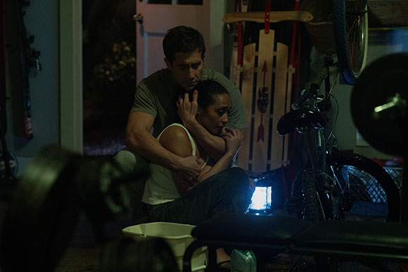 A man sits behind a woman, holding her in a close embrace in a dimly lit room.