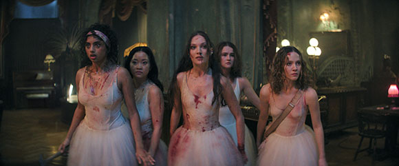 Five young women in blood-stained white dresses stand together in a dark, ornate room.