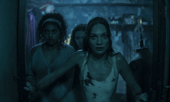 Three women with worried expressions in a dark, blue-lit room.