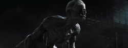 A pale, muscular, humanoid creature with textured skin leans forward in a dark environment.