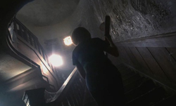 Silhouette of a person holding a long object while ascending a dark, narrow staircase.