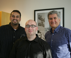 Three men standing together and smiling in an indoor setting.