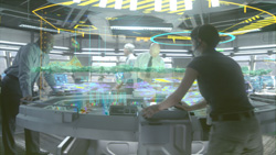 People standing around a large circular table displaying glowing holographic data and maps.