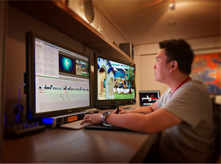 A man sits at a desk using a computer with two monitors and a digital drawing tablet.