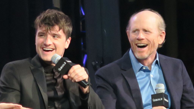 Two men sitting side by side, laughing while holding microphones during a panel.