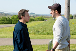Two men standing in a grassy field facing each other and talking.