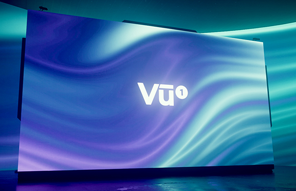 A large digital screen with blue and teal flowing wave patterns and the white text 'Vu' in the center.