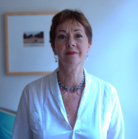 A woman with short reddish-brown hair wearing a white blouse and a blue beaded necklace.