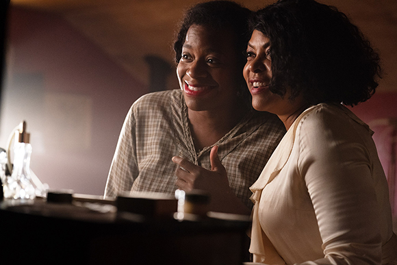 Two smiling women looking toward a light source in a dimly lit room.