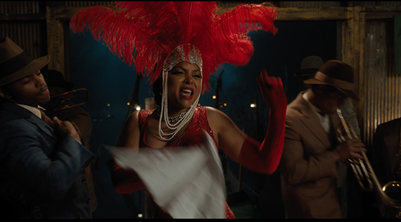 A woman in a red feathered headpiece and sequined dress performs amidst musicians in hats.