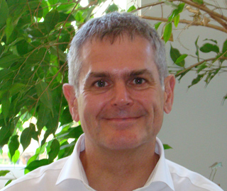 A smiling middle-aged man with short graying hair wearing a white collared shirt.