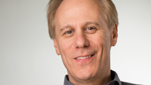 A smiling middle-aged man with light hair looking toward the camera against a plain white background.