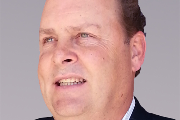 Close-up of a man with light skin and light eyes looking off-camera against a gray background.