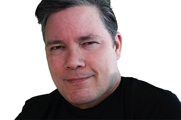 A man with short, salt-and-pepper hair and a slight smile, wearing a black shirt against a white background.