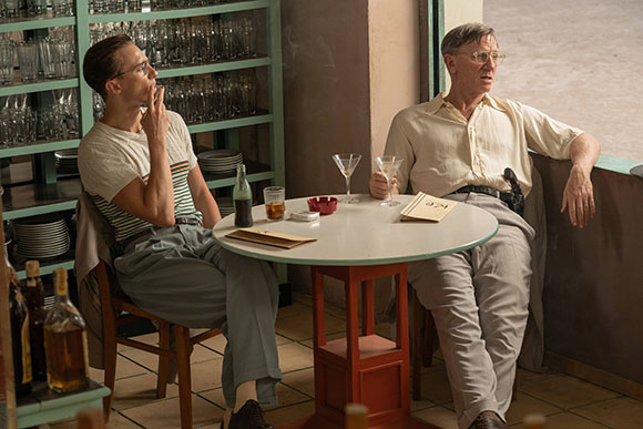 Two men sit at a round outdoor cafe table with cocktails and bottles.