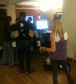 Several people stand in a dimly lit room near computer monitors and electronic equipment.