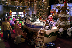 A room filled with a large Christmas tree, stuffed animals, a model boat, and various holiday decorations.