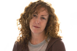 A woman with long, curly light brown hair looking forward against a white background.